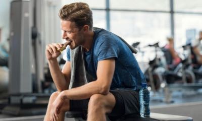 吃在健身房的汗的年轻人能量酒吧。享用巧克力的英俊的中间人以后在一个沉重的锻炼以在健身演播室。咬住快餐和基于长凳的适合的人。