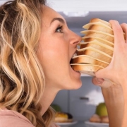 一个饥饿的女人在冰箱附近吃三明治的特写